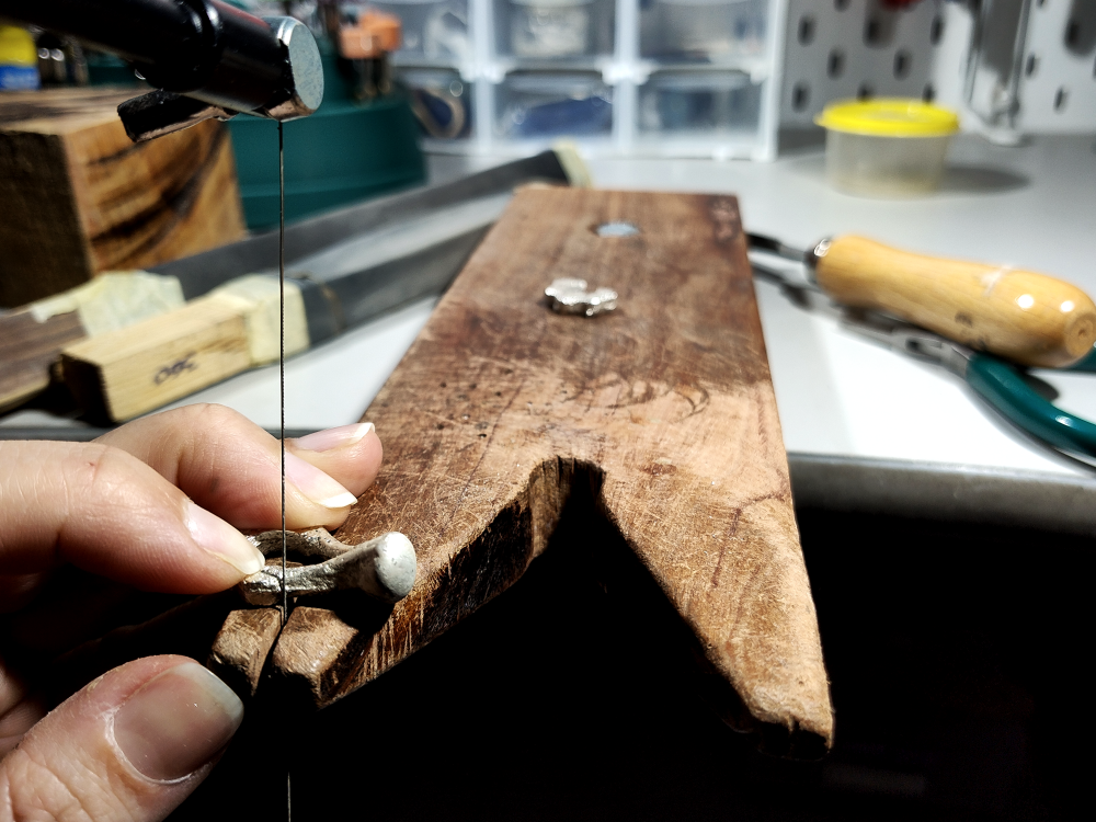 Artisan cutting and shaping silver jewellery by hand in workshop